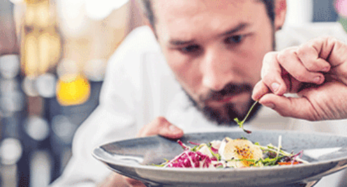 Koch richtet einen frischen Salat mit feinen Kräutern auf einem Teller an
