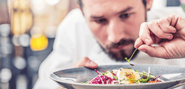 Koch richtet einen frischen Salat mit feinen Kräutern auf einem Teller an